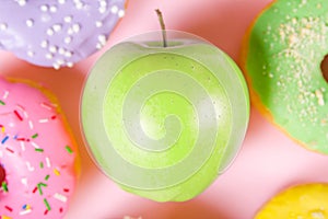 Close-up of tasty donuts and fresh green apple on pink background suggesting healthy food concept