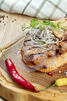 Close up on tasty Grilled Pork neck served on pita bread with onion, microgreen and hot pepper. Wooden background. Copy space.