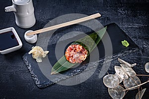 Close-up of tasty hand roll sushi with tuna and Tobico caviar served on dark stone plate with soy sauce and ginger. Copy space.