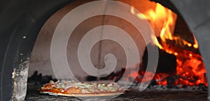 Close up of a tasty pizza being cooked inside a traditional wood fired pizza oven