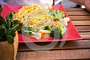 Close up of tasty spaghetti with a lot of vegetables on bright pink plate,delicious italian pasta on wooden table
