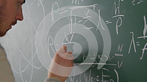 Close up teacher man hand writing math formulas on chalkboard with white chalk