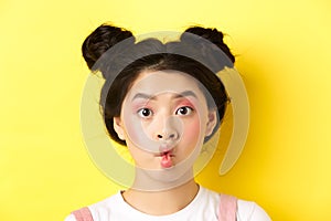 Close-up of teen korean girl pucker lips and looking funny at camera, standing with glamour makeup and stylish hairstyle