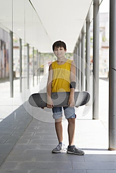 A teenage boy carrying skateboard and smiling