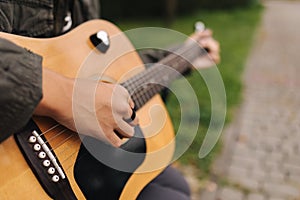 Close-up of teenage boy playing guitar. Male finger on strings. Boy play music. Autumn mood outdoors