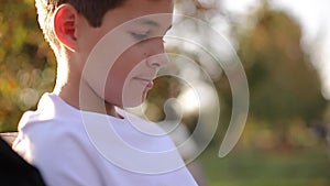 Close up of Teenage boy in white sweater sitting on the bench. Handsome school boy with backpack in autumn park