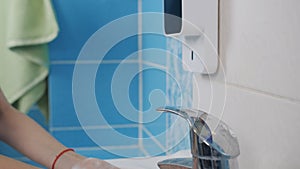 Close-up of a teenage girl washing her hands with an automatic soap dispenser in the bathroom.
