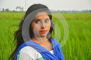 Close up of teenage girl wearing golden nose pin and ear rings with white cotton salwar kameez standing in a paddy field, selectiv