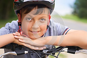 Close-up of a teenager boy in protective helmet sitting on his bicycle and keeps his head on his hands resting on the