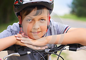 Close-up of a teenager boy in protective helmet sitting on his bicycle and keeps his head on his hands resting on the