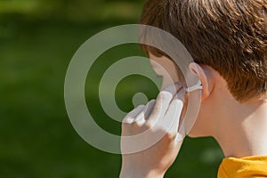 Close up of teenager boy using earbuds outdoor. Lifestyle boy wearing wireless earphones, listening song or audiobook on