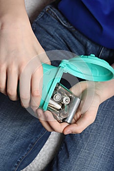 Close-up of a teenager pouring used batteries from a small bin into their hand, promoting recycling