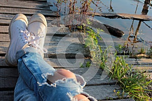 Close up of teenager`s feet in modern and trendy white sneakers and ripped jeans. Sunny summer day.