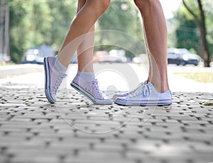 A close-up of teenages` legs in white sneakers standing on a blurred natural background. Copy space. Outdoors concept.