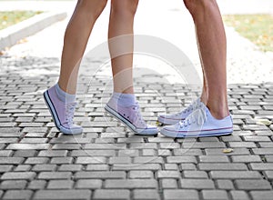 A close-up of teenages` legs in white sneakers standing on a blurred natural background. Copy space. Outdoors, youth