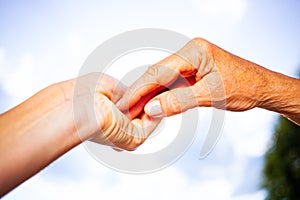 close-up of tender gesture between two generations. Young woman holding hands with a senior lady. Blue sky background