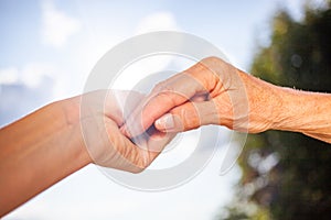 close-up of tender gesture between two generations. Young woman holding hands with a senior lady. Blue sky background