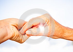 close-up of tender gesture between two generations. Young woman holding hands with a senior lady. Blue sky background