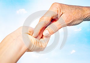 close-up of tender gesture between two generations. Young woman holding hands with a senior lady. Blue sky background