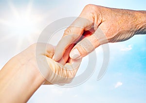 close-up of tender gesture between two generations. Young woman holding hands with a senior lady. Blue sky background