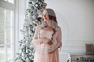Close-up tenderness female hand hugging pregnant tummy feeling fondness at Christmas tree photo