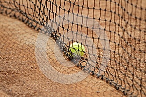 Close up tennis ball and net on court. Close up of tennis ball on clay court. Red clay court