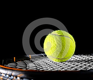 Close up of tennis ball on string or net of tennis racquet, racket, on black background for sport for exercise hobby and lifestyle