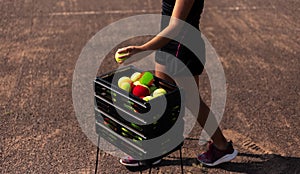 Close-up of tennis teenage girl near box of balls on court.