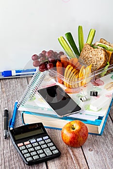 Close up of a textbook and notebook surrounded by other school supplies and a lunch kit on top.