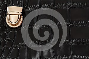 Close-up texture of black handbag from genuine leather with embossed under the skin of reptile, gold lock. Concept of