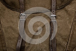 Close-up texture of a canvas fabric backpack. Leather straps and metal buckles. Vintage khaki back