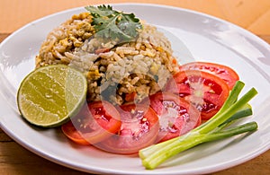 Close up Thai food, fried rice with eggs and pork served with fresh tomato slice, spring onions and lemon slice on white plate.