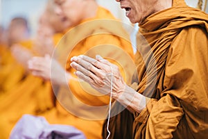 Close up of Thai monk praying focus at hand with white rope.