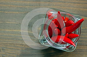 Close up of Thai red fresh hot chilli peppers in a glass vintage jar, blurred brown background. Food pattern. Popular spices