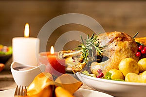 Close up of thanksgiving table with roast chicken, vegetables, candles and autumn decoration