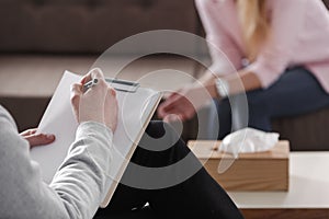 Close-up of therapist hand writing notes during a counseling session with a single woman sitting on a couch in the blurred