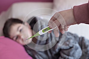 Close-up thermometer. Mother measuring temperature of her ill kid. Sick child with high fever laying in bed and mother