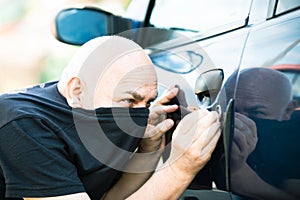 Close up thief stealing car. Unlocked car, man trying to break into inside. The man dressed in black with a balaclava on