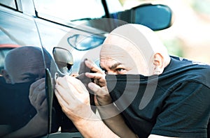 Close up thief stealing car. Unlocked car, man trying to break into inside. The man dressed in black with a balaclava on