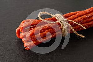 Close-up of thin dry smoked sausage kabanos or cabanossi on a black stone serving board. Traditional polish meat delicacy