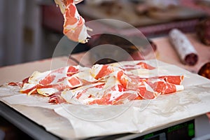 Close-up of thin slices of Italian ham, prosciutto crudo weight on scale, grocery store. Real scene in supermarket