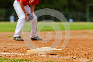 Close up of the third baseball base and a foul line with grass outfield in the background. Baseball diamond