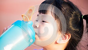 Close up of thirsty girl drinking clean water. Cute kid holding a blue bottle of water.