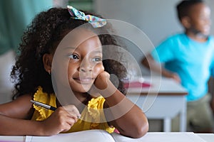 Close-up of thoughtful african american elementary schoolgirl sitting at desk in classroom