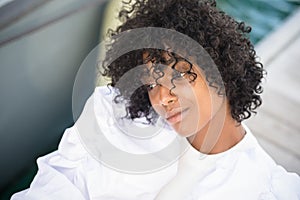 Close up of thoughtful african american woman with curly hair looking away on boat. Beautiful black woman in white dress deep in