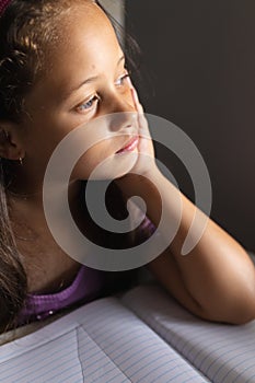 Close-up of thoughtful caucasian elementary schoolgirl with hand on chin looking away in classroom