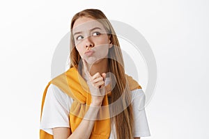 Close up of thoughtful young woman, making pensive face, touching chin and pucker lips, looking at upper right corner