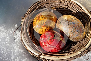 Close-up of three brightly colored eggs shining in the sun in a rattan nest on snow photo