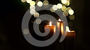 Close up of three burning candles with blurred Christmas light background. In the frame flashes a dark shadow, closing