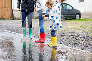 Close-up of three children, toddler girl and two kids boys wearing red, yellow and green rain boots and walking during
